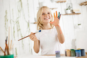 Kid enjoying painting with colorful paint on her hands, smiling and having fun.