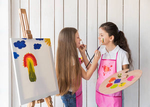 Two teenage girls discussing art while holding a board and standing in front of a canvas.