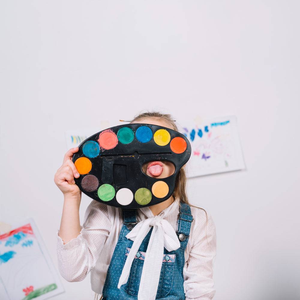 kid’s face covered with colorful paint on a painting board